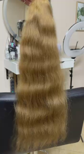 Video showing the flexibility and shine of a 65 cm (26 inch) premium raw Slavic wavy hair extension in cold-bleached Honey Blonde color